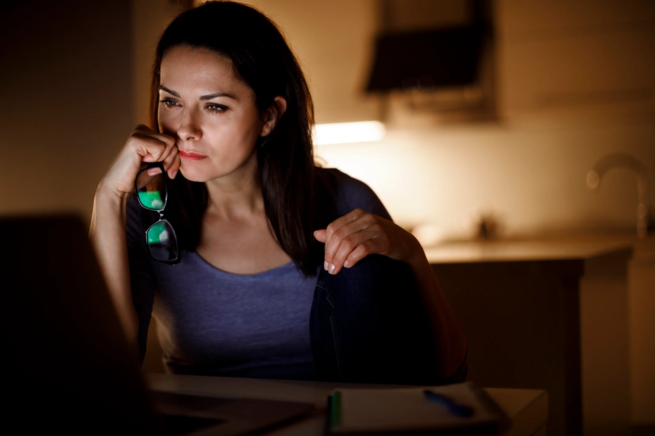A woman holding her glasses off her face staring at her computer screen